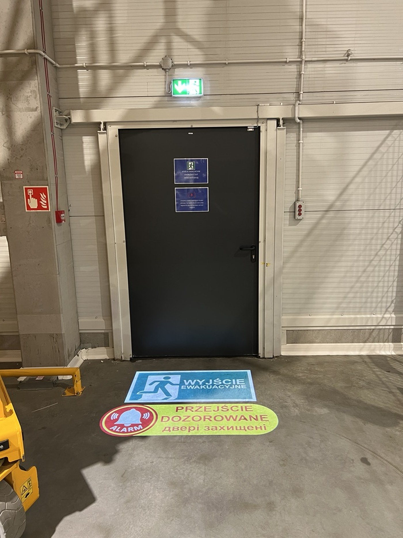 Two messages projected in front of an emergency exit door: Emergency exit and Monitored door, in Polish and Ukrainian