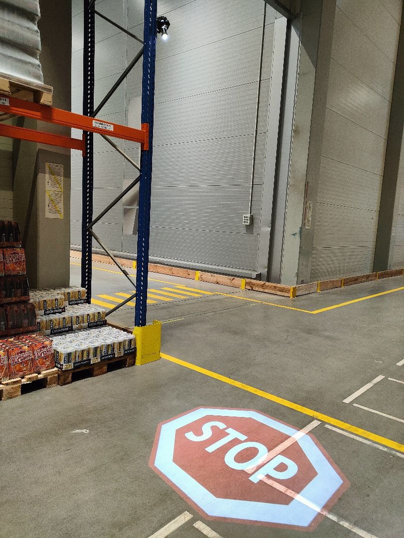 A STOP sign projected onto the floor at the exit from a racking aisle, beside a dock door