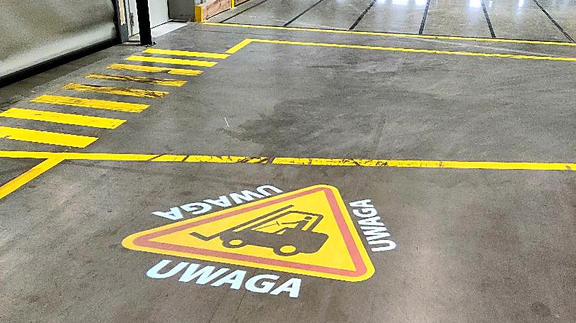 Znak ostrzegawczy o wózkach wyświetlony na posadzce przed bramami doku