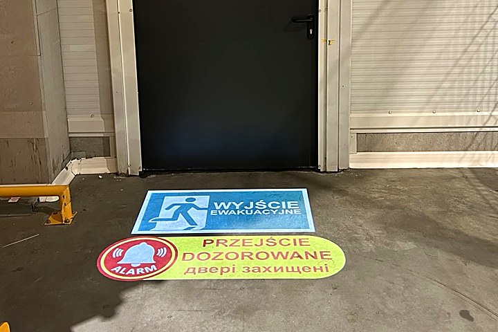 Znak wyjścia ewakuacyjnego i komunikat o przejściu dozorowanym wyświetlone po polsku i ukraińsku